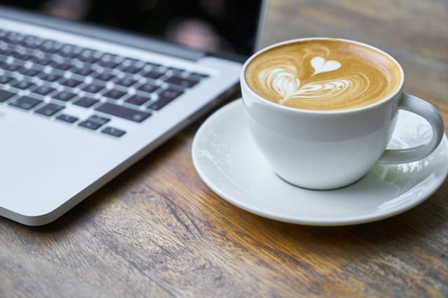 a cup of coffee with a heart figure on top of it next to a laptop