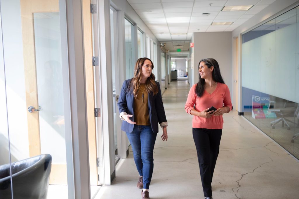 two woman talking while walking in an office