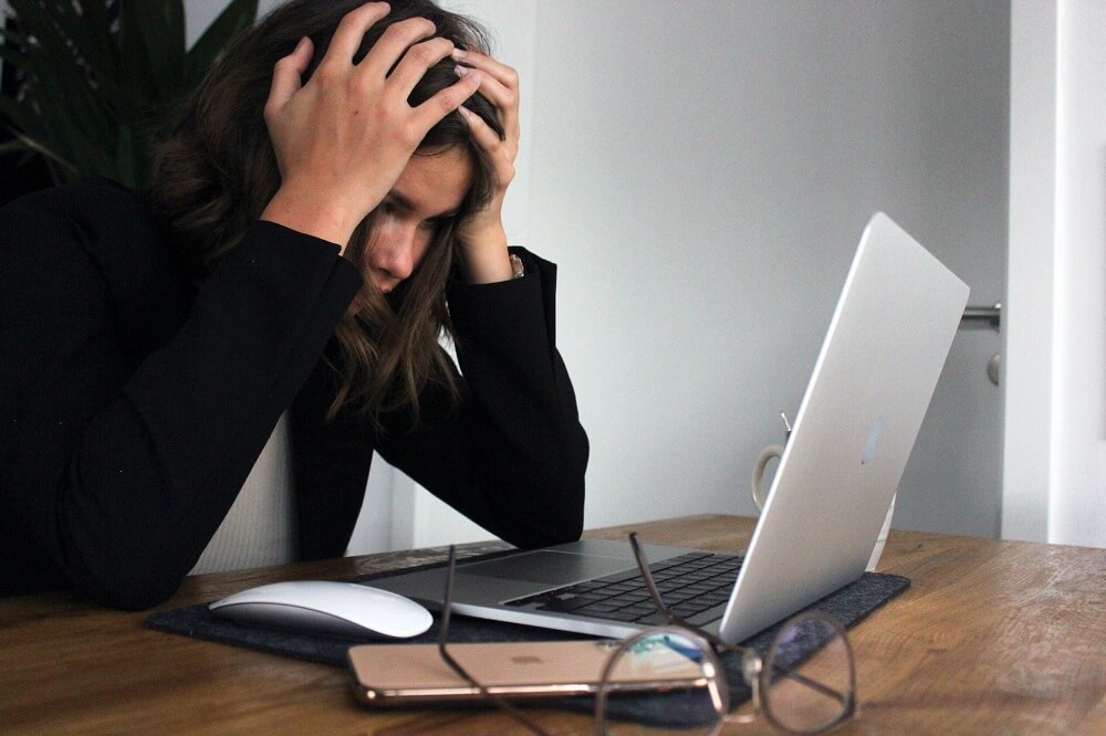 photo of a worker with her head in her hands in front of her laptop illustrating employee burnout
