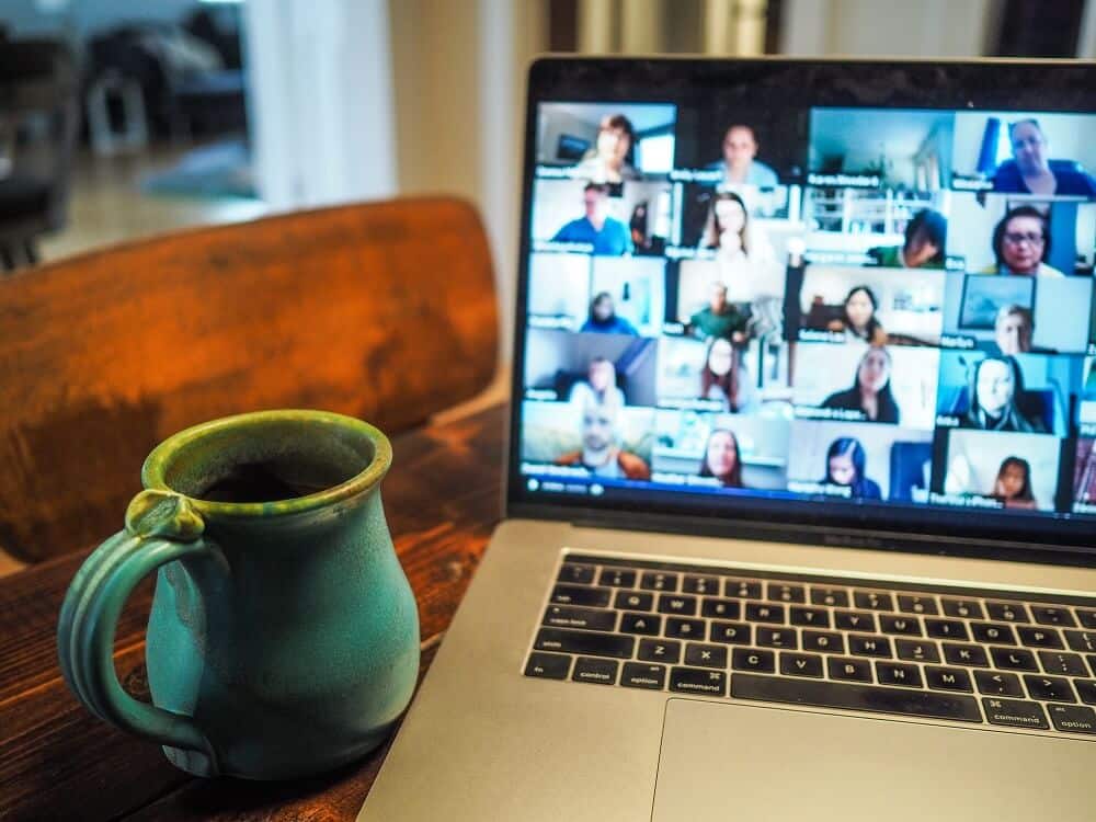 photograph of a coffee mug beside a laptop showing multiple attendees of a Zoom call to illustrate virtual meeting fatigue